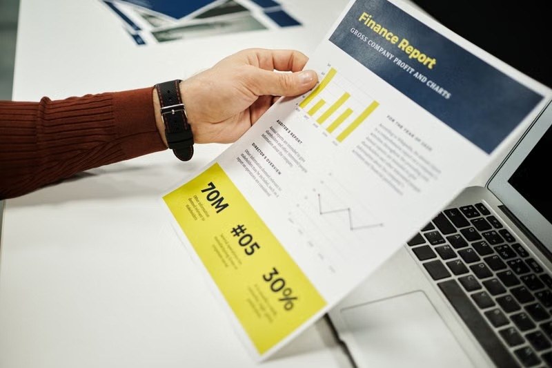 Hand holding a finance report beside a laptop